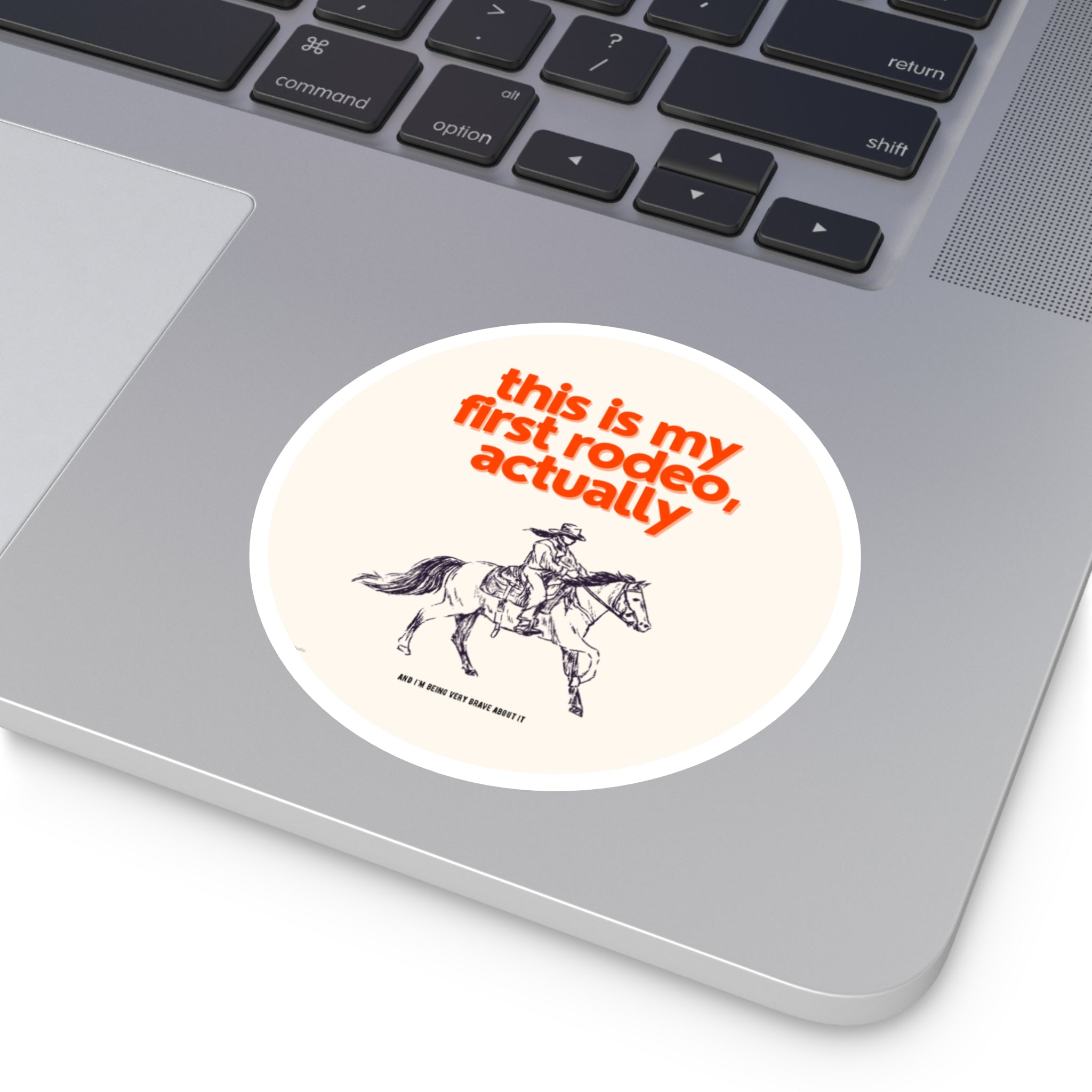 Laptop with a sticker featuring a cowboy and text 'This is my first rodeo, actually' on a white background.